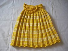 a yellow and white plaid skirt with a bow at the waist, sitting on top of a bed