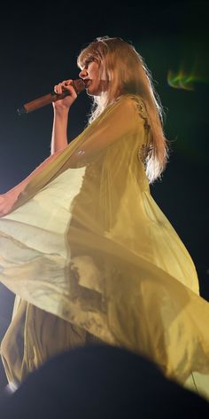 a woman in a white dress holding a microphone and singing into the air at a concert