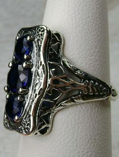 "Simulated Blue Sapphire Ring 3Stone Rectangle#60 Custom Made This is a lovely late Victorian era reproduction ring in solid sterling silver. The gorgeous filigree ring is set with 3 round-cut simulated blue sapphire gemstones. The 2 smaller blue sapphire gems are 4.5mm in diameter, and the center one is 6mm in diameter. This filigree setting is a casting from an actual Antique ring; notice the amazing etched band... The ring sits 3/4th\" (19mm) NS on the finger. The quality of the silver and ge Formal Sterling Silver Ring With Rectangular Stone, Sterling Silver Ring With Rectangular Stone For Formal Events, Sterling Silver Rings With Rectangular Stone For Formal Events, Sterling Silver Rings With Rectangular Stone For Formal Occasions, Formal Sterling Silver Sapphire Ring With Rectangular Stone, Silver Sapphire Ring With Rectangular Gemstone, Formal Sapphire Ring With Rectangular Sterling Silver Stone, Formal Rectangular Sapphire Ring In Sterling Silver, Blue Three Stone Emerald Cut Jewelry