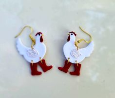 two pairs of white and red rooster shaped earrings on a counter top with gold ear wires