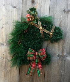 a christmas wreath hanging on the side of a wooden fence with pine cones and bows