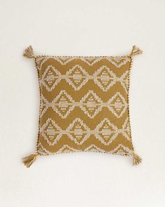 a brown and white pillow with tassels on the front, sitting against a white wall