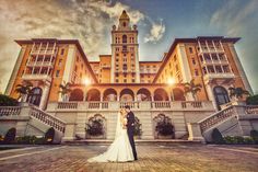 a bride and groom standing in front of a large building with stairs leading up to it