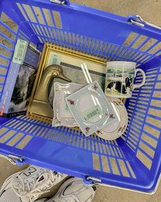 a blue shopping basket filled with items on top of a floor next to a pair of shoes