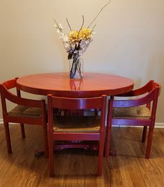 a vase with flowers sitting on top of a wooden table next to two red chairs