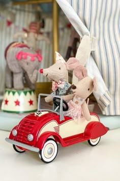 two stuffed animals are riding in an old fashioned red toy car with another animal behind them