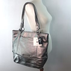 The Silver Pewter Hue Of The Leather And Silver-Tone Hardware Lends An Air Of Understated Elegance, Allowing This Purse To Effortlessly Complement A Wide Range Of Outfits. The Supple Leather Is Not Only Visually Appealing But Also Incredibly Soft To The Touch. The Animal Print Inside Has A Zipped Divider, Several Utility Pockets On One Side, And A Zipper Compartment On The Other Side. Designed With The Modern Woman In Mind, This Tote Bag Offers Ample Space Without Compromising On Style. The Room Elegant Silver Bag For Everyday Use, Elegant Silver Bag For Everyday, Elegant Everyday Silver Bag, Elegant Silver Everyday Bag, Everyday Silver Shoulder Bag With Palladium Hardware, Silver Shoulder Bag With Palladium Hardware For Everyday, Silver Shoulder Bag With Silver-tone Hardware For Shopping, Silver Tote Shoulder Bag With Silver-tone Hardware, Silver Bag With Silver-tone Hardware For Shopping