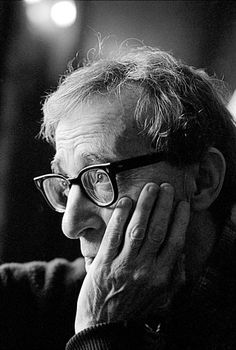 a black and white photo of a man with glasses looking off to the side while holding his hand on his face