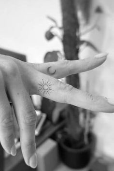 two fingers with small tattoos on them, one has a sun and the other has an arrow