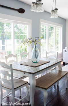 a dining room table with chairs and a bench in front of the large windows that look out onto the yard