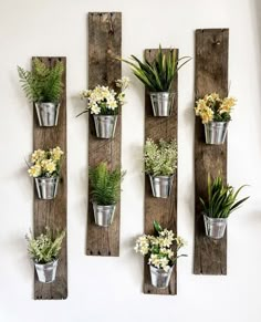 several metal buckets filled with flowers hanging from wooden planks on a white wall