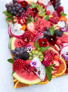 sliced fruit arranged on top of each other with leaves and flowers in the middle, including grapes, watermelon, kiwi, raspberries, oranges