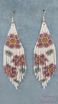 two pairs of beaded earrings with fringes on blue fabric background, one is white and the other is pink