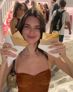 a woman is holding some food in her hands and posing for the camera with other people behind her