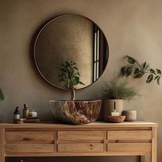 a wooden table with a round mirror above it and plants on the wall behind it