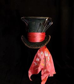 a top hat with red ribbon tied around it on a black background, next to an orange and pink scarf