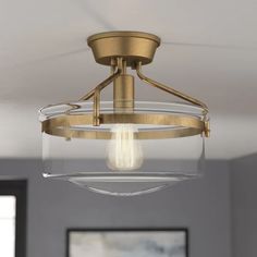 a semi - flush ceiling light fixture with clear glass and brass finish, hanging in a living room