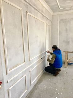 a man kneeling down in front of a white wall and pointing at something on the wall