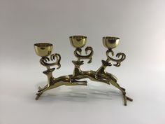 three brass candlesticks sitting next to each other on a white surface with one candle holder in the shape of an antelope