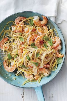 a pan filled with pasta and shrimp on top of a white table next to a napkin