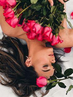 a woman laying on top of a bed with pink roses around her neck and head