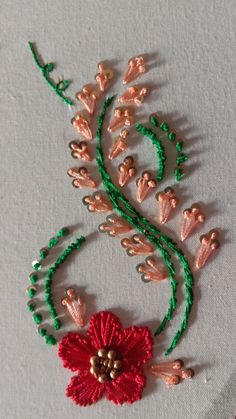 a red flower with green stems on a white table cloth next to beaded beads