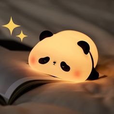 a panda bear lamp sitting on top of a bed next to an open book with the light turned on