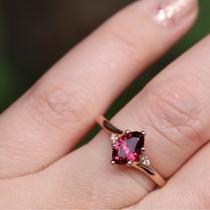 a woman's hand holding a ring with a pink stone in it and diamond accents