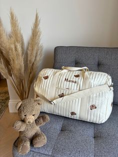 a teddy bear sitting on a couch next to a white quilted duffel bag