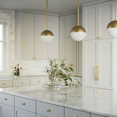 a kitchen with marble counter tops and gold accents on the lights over the sink is surrounded by white cabinetry