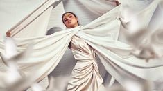 a woman in white dress standing with her hands on the fabric draped over her head