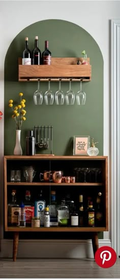 a bar with wine glasses and liquor bottles on the top shelf, next to a vase filled with flowers