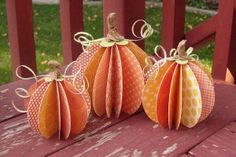 three paper pumpkins sitting on top of a wooden bench