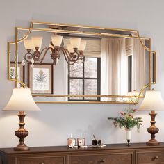 a mirror hanging on the wall above a dresser with two lamps and a lamp shade