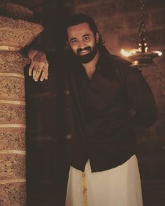 a man with a beard standing next to a stone pillar and holding his hand on the wall