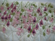 pink flowers and green leaves are embroidered on white material with beadwork in the center