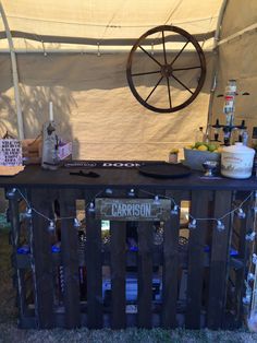 a bar made out of pallets with bottles on top and lights strung from it