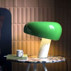 a green lamp sitting on top of a table next to a white cup and book