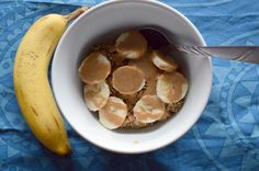 a banana and some food in a white bowl on a blue cloth with a spoon