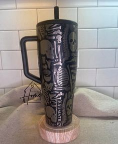 a black and white coffee mug with skeleton images on it sitting on a wooden stand