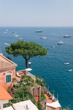 boats are floating in the water near some buildings and trees on top of a hill