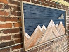 a wooden sign on the side of a brick building with mountains painted on it's sides