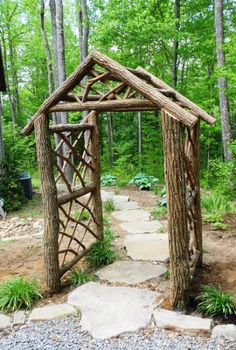 a wooden structure made out of branches in the middle of a forest with rocks and gravel