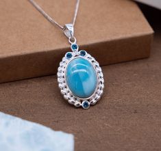 Discover the epitome of sophistication with our Oval Silver Pendant featuring a captivating Larimar center stone. This pendant seamlessly marries classic design with intricate detailing, creating an accessory that transcends trends. Oval Larimar Centerpiece: The focal point of this pendant is an exquisite oval Larimar stone, celebrated for its serene blue hues. Embraced by a silver setting, the Larimar takes center stage, infusing the piece with a tranquil and timeless allure. Intricate Heart-Shaped Frame: Surrounding the Larimar is a meticulously crafted oval silver frame. Comprising an array of small silver heart shapes interconnected in an artistic pattern, this frame adds a touch of romance and femininity to the design. Blue Topaz Accents: Three blue topaz stones are delicately studded Blue Topaz Oval Pendant Jewelry, Blue Topaz Gemstones For Gifts, Oval Pendant Jewelry With Accent Stones For Gift, Elegant Larimar Pendant Jewelry, Blue Topaz Oval Pendant Necklace, Blue Topaz Oval Pendant Necklace For Anniversary, Blue Topaz Oval Pendant Necklace With Birthstone, Oval Pendant Jewelry With Gemstone Accents For Wedding, Blue Topaz Birthstone Necklace With Oval Pendant