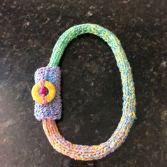 a knitted bracelet with a button on it sitting on top of a black surface