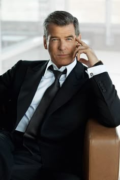 a man in a suit and tie sitting on a chair with his hand to his ear