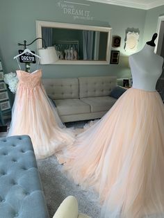 two dresses are on display in front of a couch and mirror, one is peach