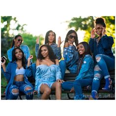 a group of young women sitting on top of a wooden bench in front of trees