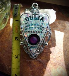 "This is a Ouija Board Mood Color Change Resin Faux White Opal Planchette Hand Made Necklace. It features a hand cast resin planchette with faux opal prismatic flakes that has a glass mood stone for the \"viewer\". It is set on a 3 inch antiqued silver tone setting. It comes with an 18 inch stainless steel chain. If you need the chain longer or shorter please let me know in the notes section of your order. This necklace is hand made by me. The \"viewer\" on the necklace is a glass mood stone tha Magical Silver Resin Jewelry, Silver Resin Jewelry With Magical Style, Board Mood, Mood Stone, Mood Colors, Ouija Board, Resin Projects, Hand Cast, White Opal