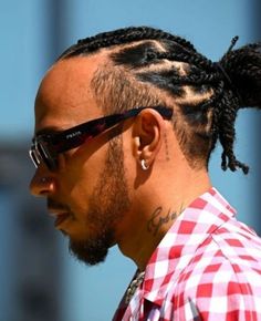 a man with dreadlocks wearing sunglasses and a checkered shirt looks off to the side